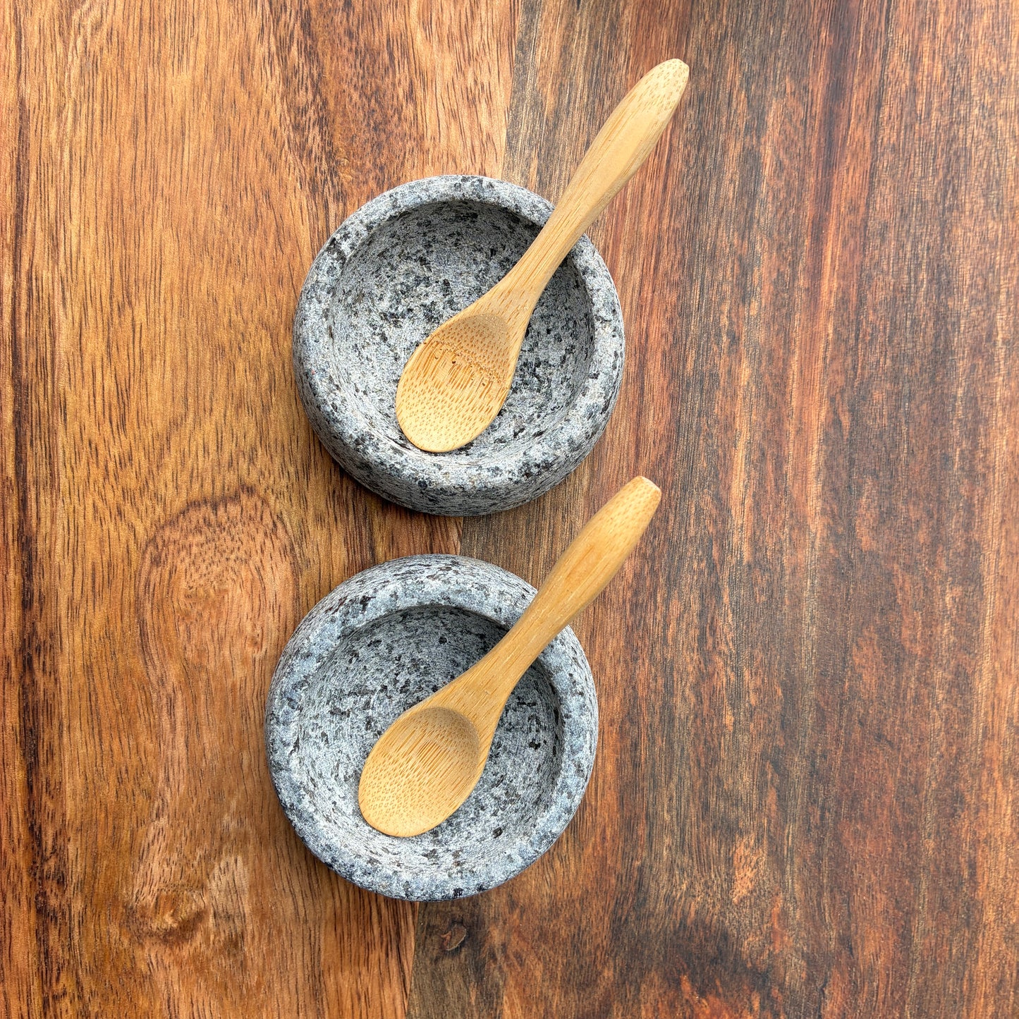 Two stone bowls with wooden spoons on a wooden surface