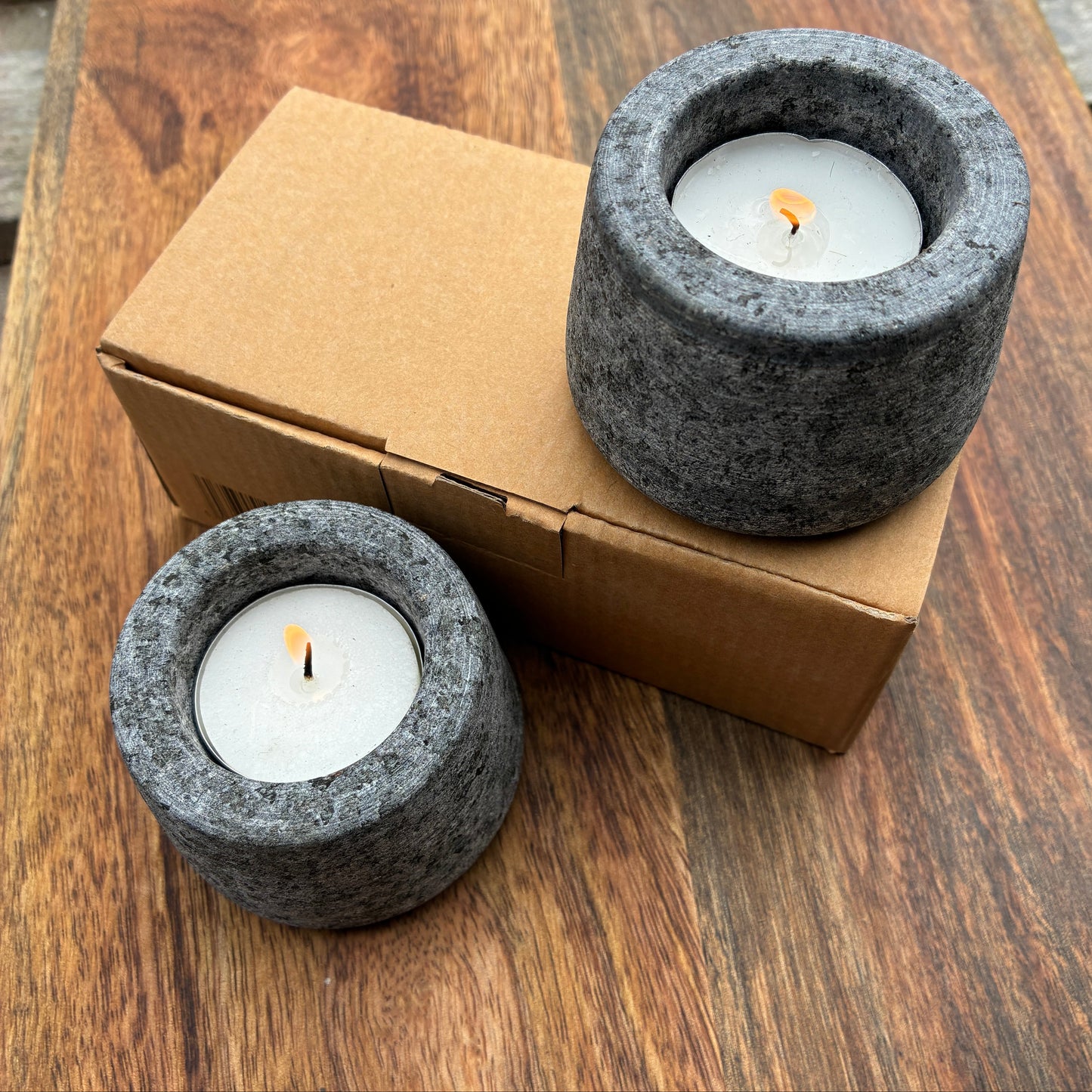 Two grey stone candle holders with candles on a wooden surface.