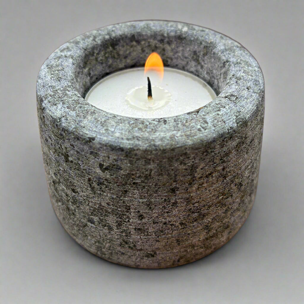 Candle in a gray stone holder on a grey surface