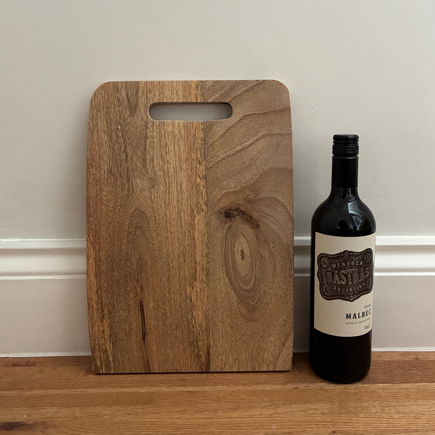Wooden cutting board with a bottle of wine on a wooden surface against a beige wall.
