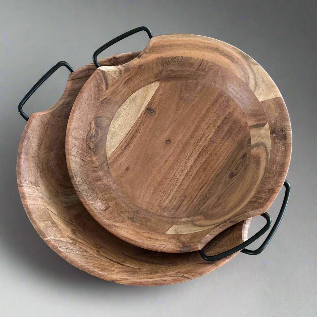 Two wooden bowls with black handles on a light wood surface.