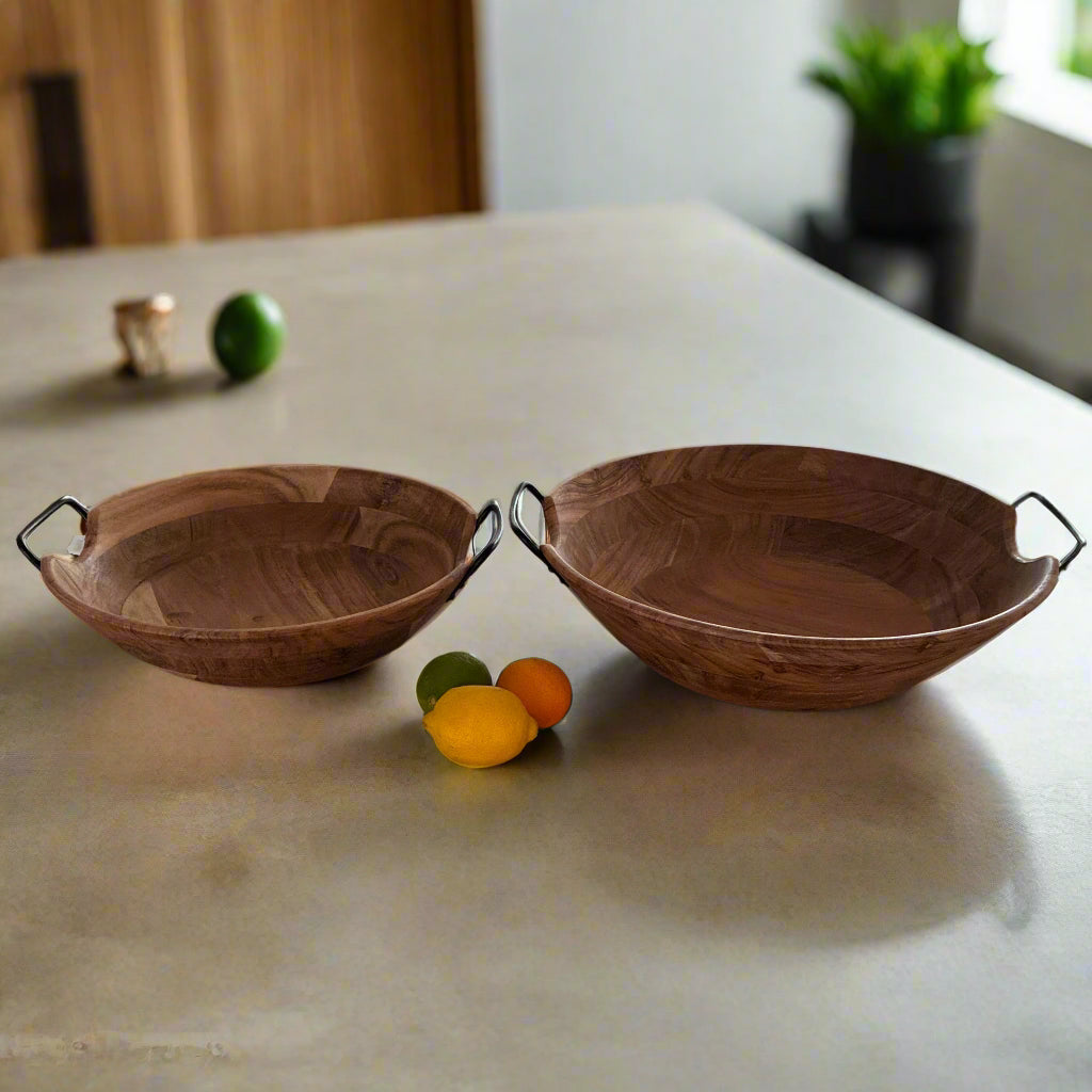 Two wooden bowls on a kitchen island with a laptop and fruits in the background.