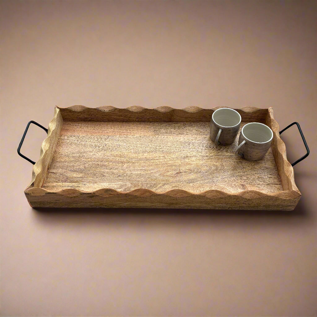 Wooden tray with wavy edge and black handles on a wooden floor.