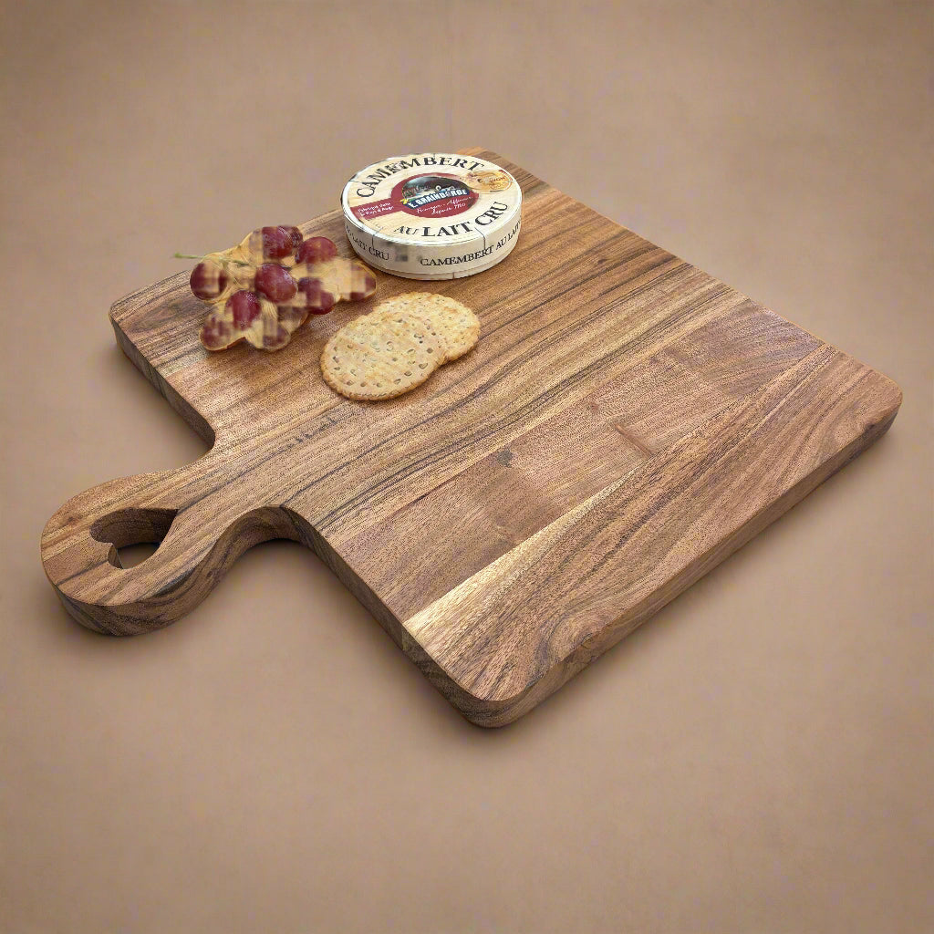 Wooden cutting board with grapes, crackers, and a container of Camembert cheese on a gray wooden floor.