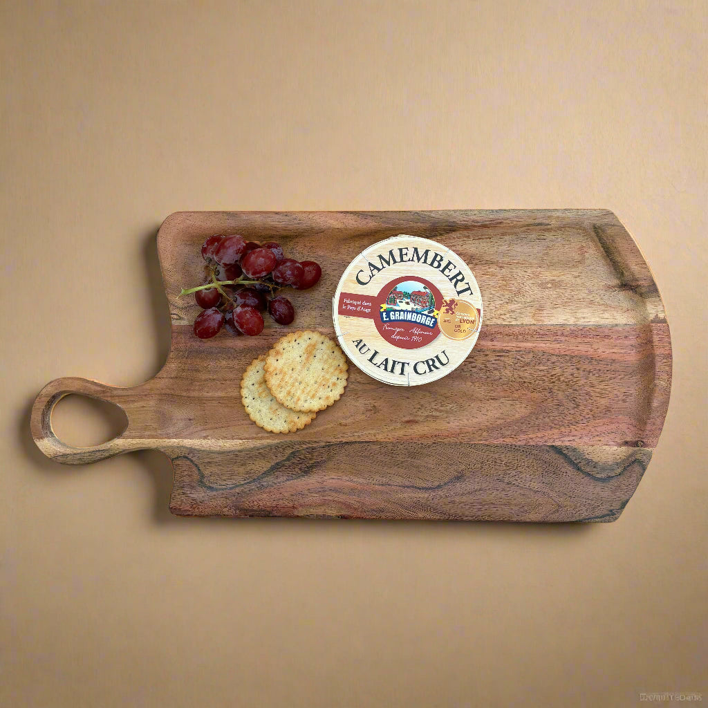 Wooden cutting board with Camembert cheese, grapes, and crackers on a gray wooden floor.