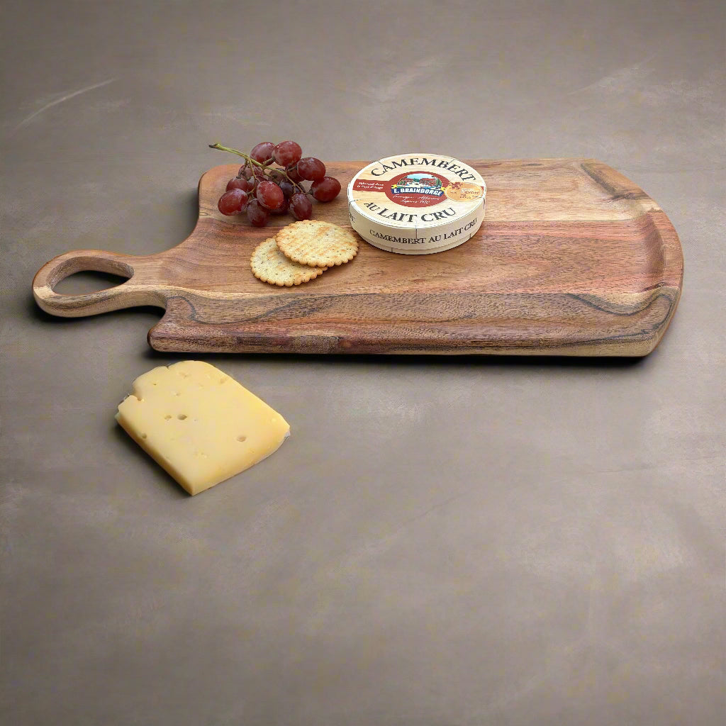 Wooden cutting board with cheese, crackers, and grapes on a gray wooden floor.