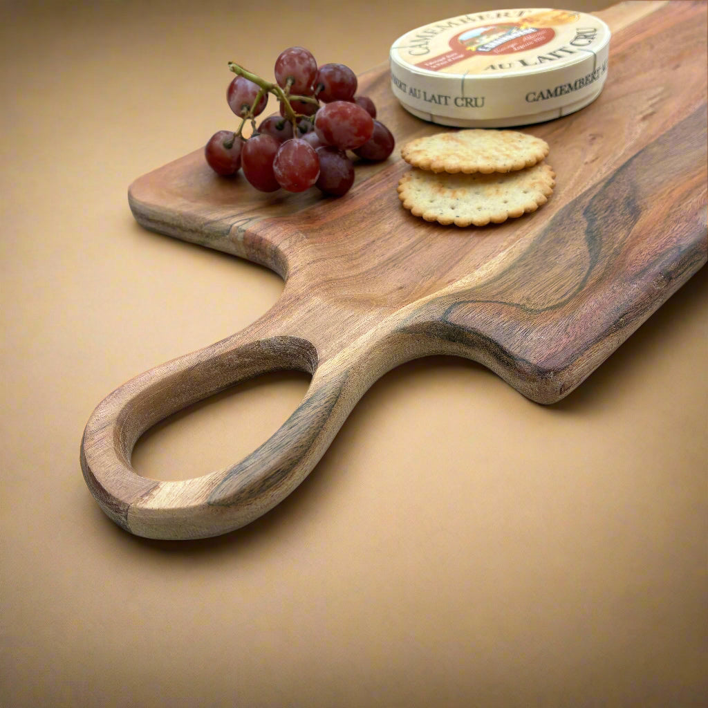 Wooden serving board with grapes, crackers, and a wheel of cheese on a light wooden surface.