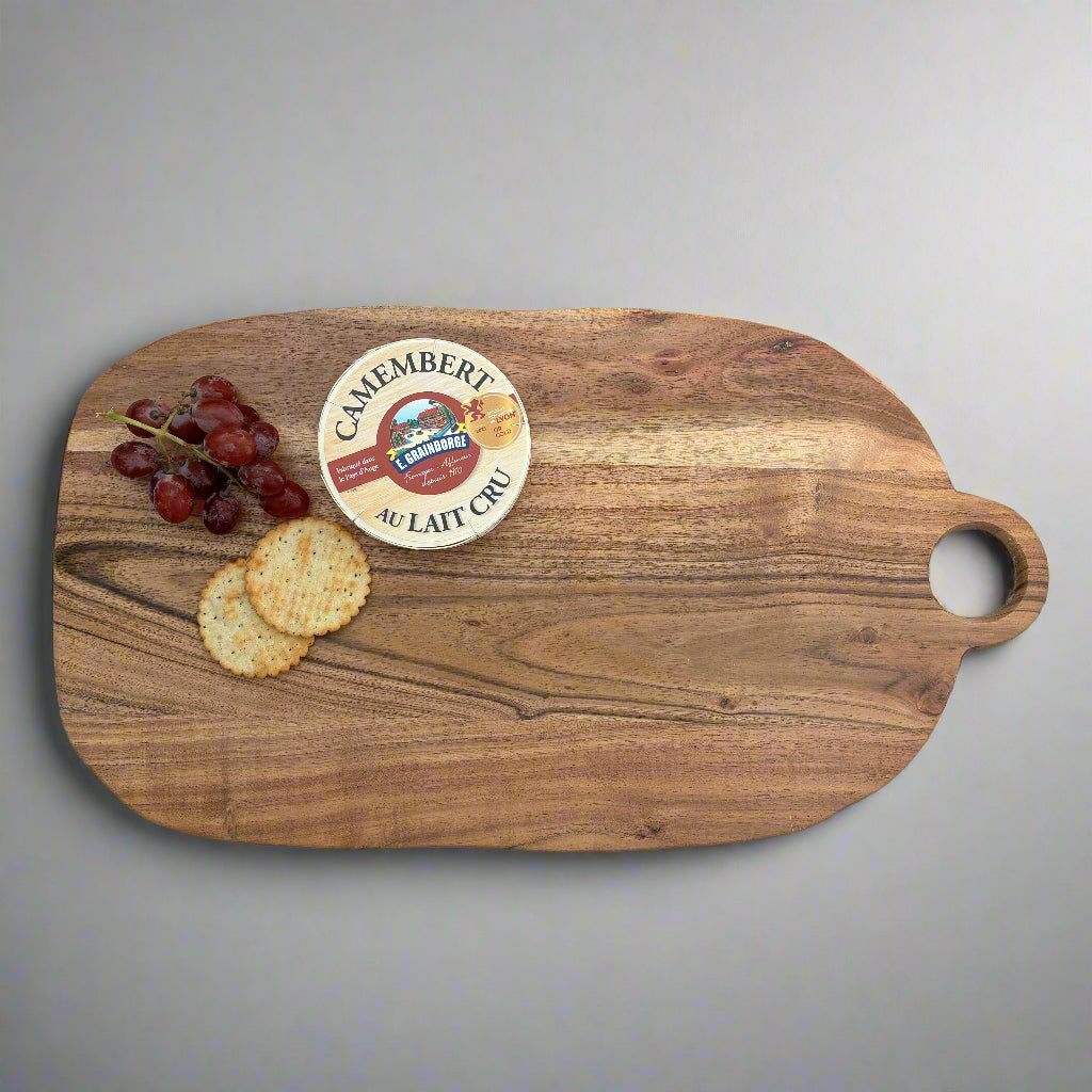 Wooden cutting board with Camembert cheese, grapes, and crackers on a wooden floor.