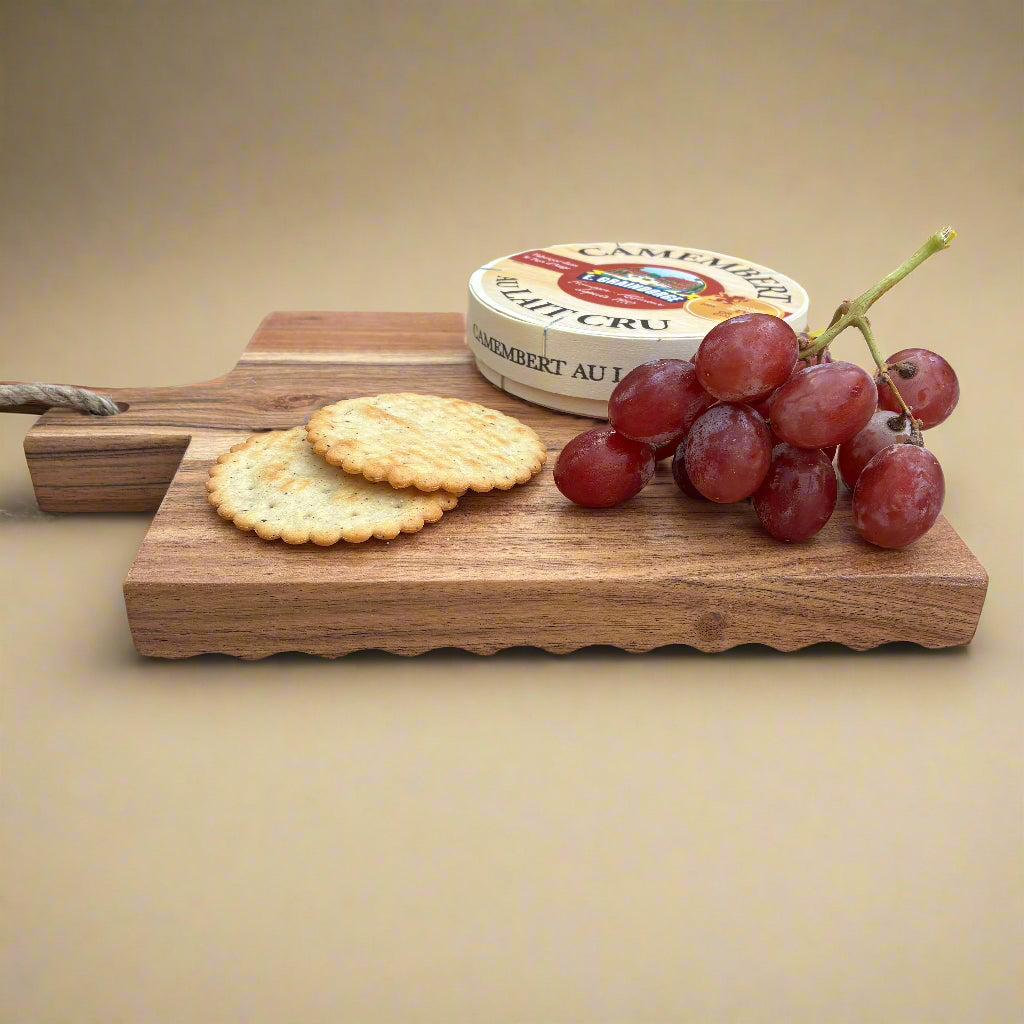 Wooden cutting board with Camembert cheese, crackers, and grapes on a wooden surface.