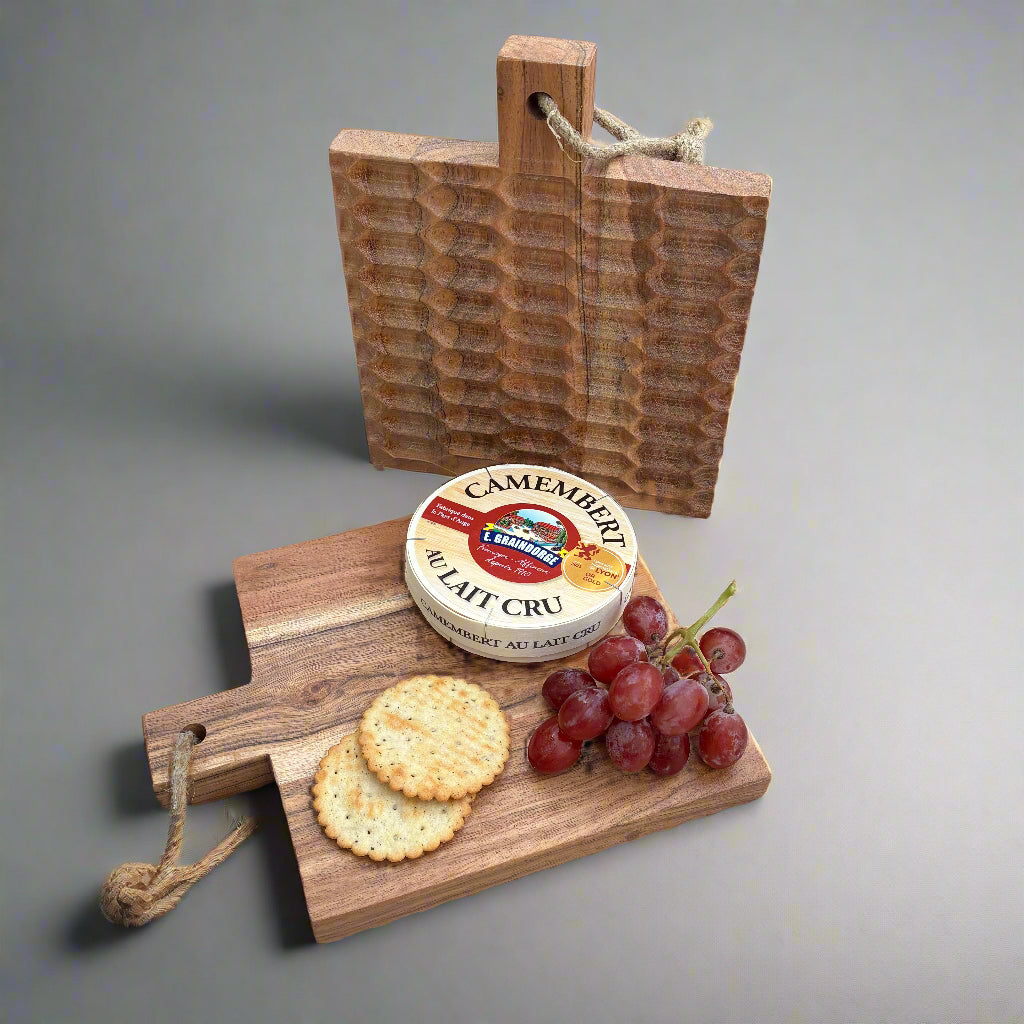 Wooden cutting board with Camembert cheese, crackers, and grapes on a wooden floor.