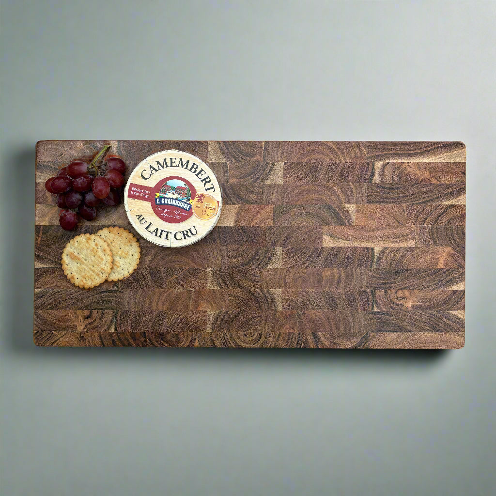 Wooden cutting board with Camembert cheese, grapes, and crackers on a gray wooden floor.