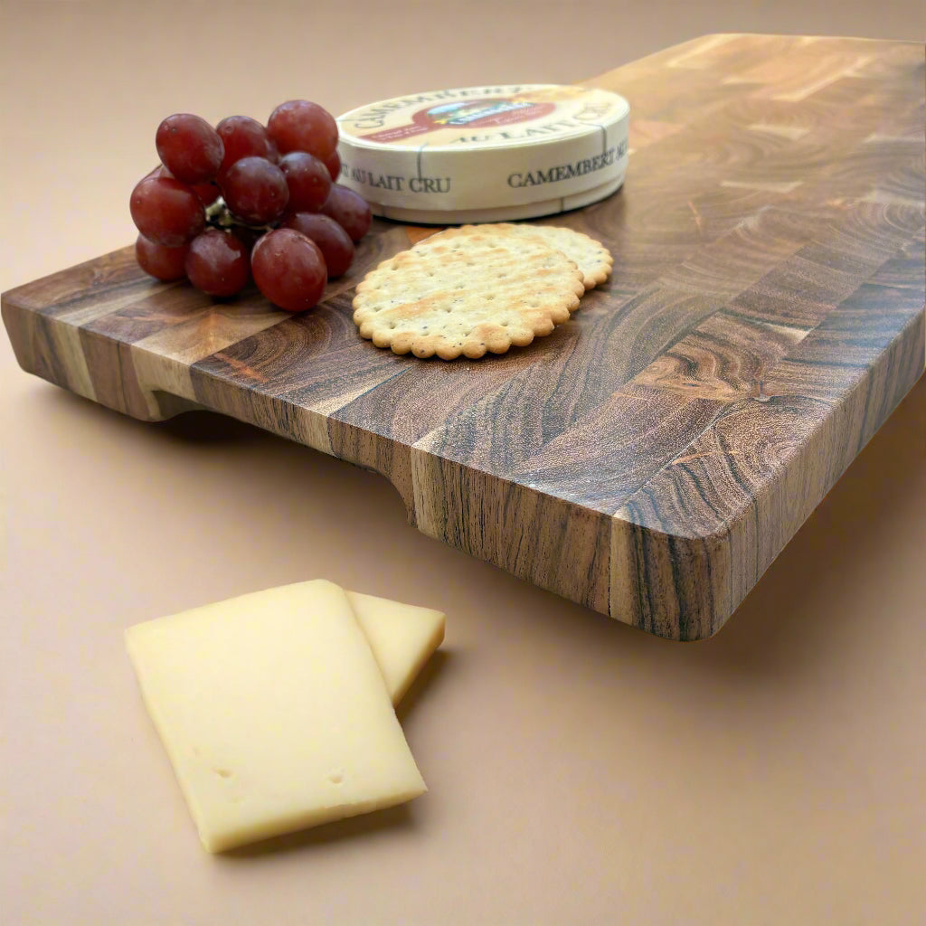 Wooden cutting board with grapes, cheese, and crackers on a wooden surface