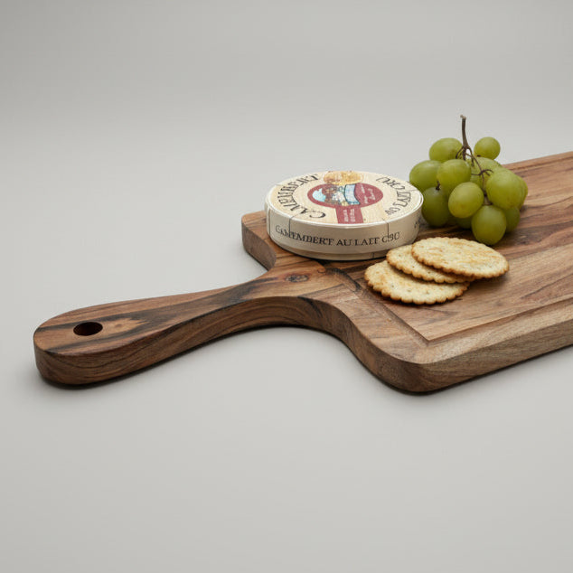 Wooden cheese board with a wheel of cheese, crackers, and grapes on a gray wooden surface.