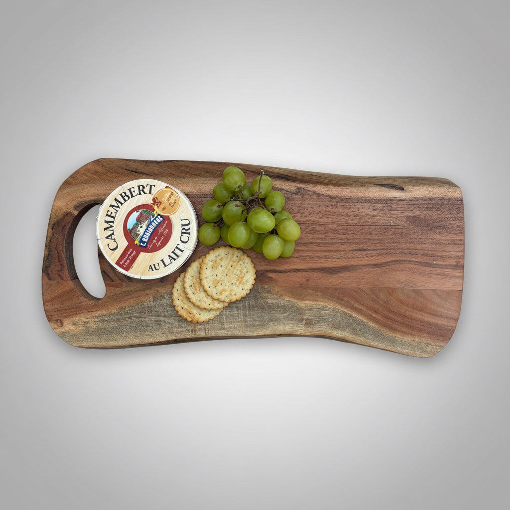 Wooden cutting board with Camembert cheese, crackers, and grapes on a gray wooden floor.