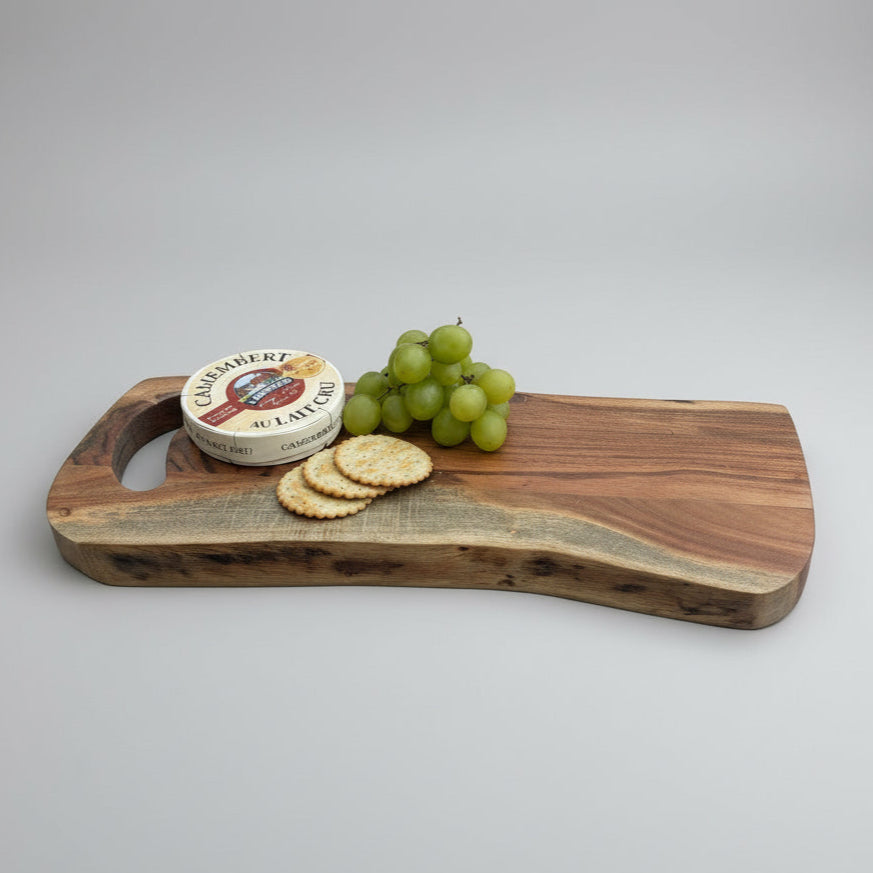 Wooden cutting board with cheese, crackers, and grapes on a gray wooden floor.