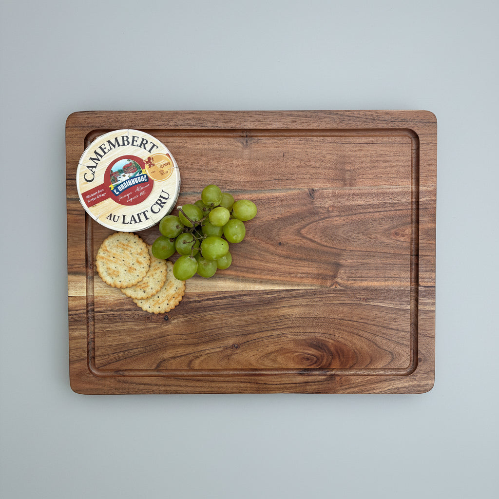 Wooden cutting board with grapes, crackers, and a wheel of cheese on a gray wooden floor.
