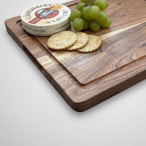 Wooden cutting board with Camembert cheese, crackers, and grapes on a light gray surface
