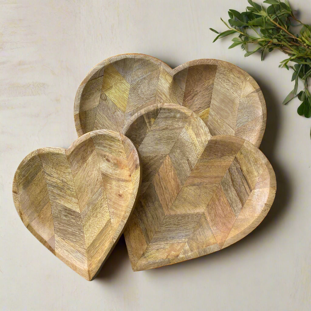 Set of three wooden heart-shaped bowls on a light background with greenery.