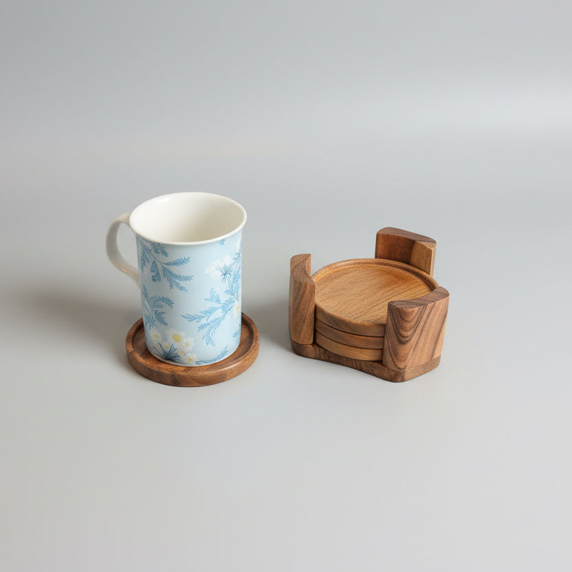 White mug with blue design on a wooden coaster next to a wooden bowl on a gray surface.