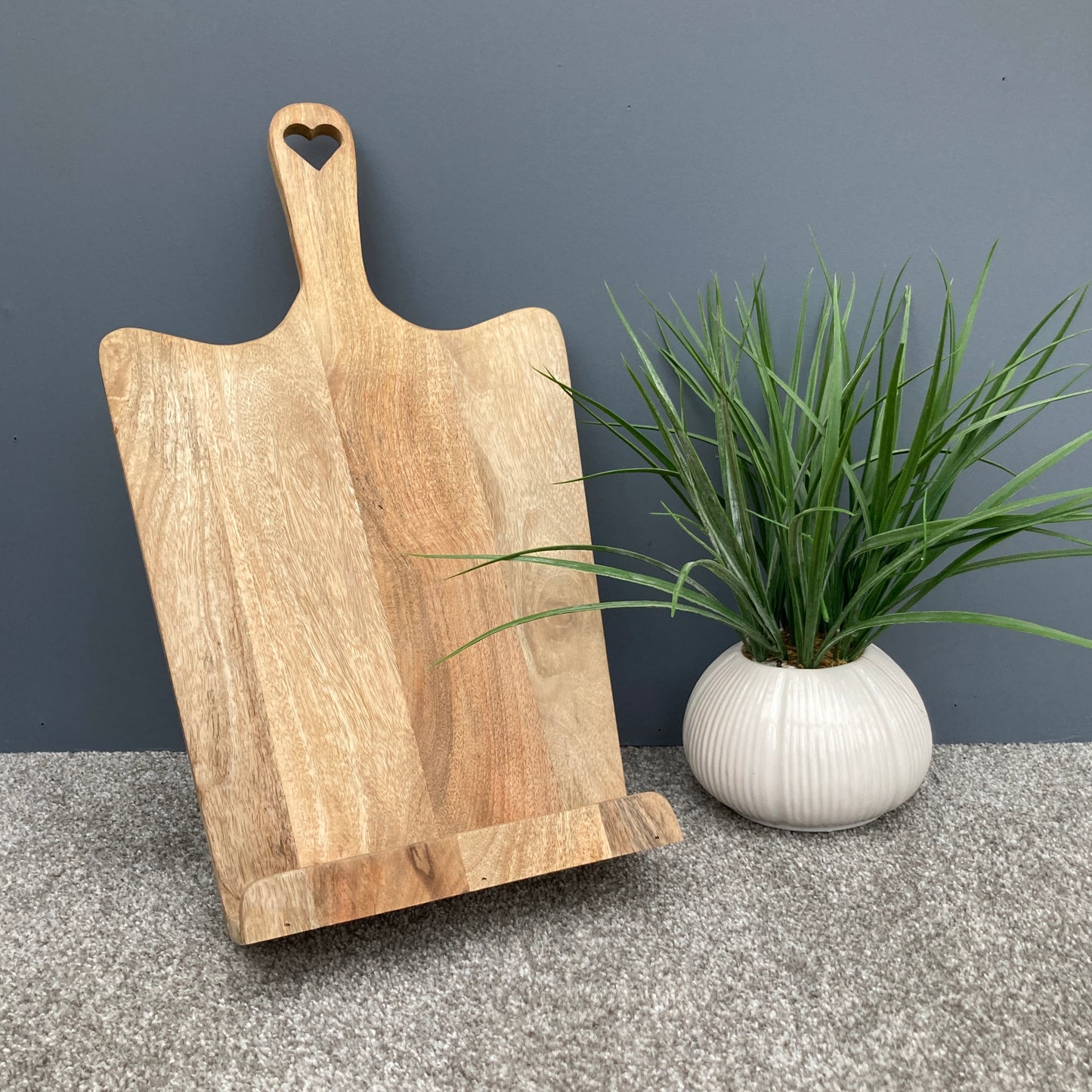 Tall Mango wood recipe stand with cut out heart handle next to plant.