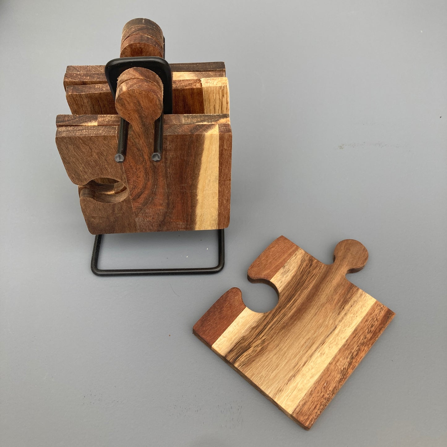 Set of 6 Acacia wood puzzle shaped coasters on a metal holder. View of coaster and holder.
