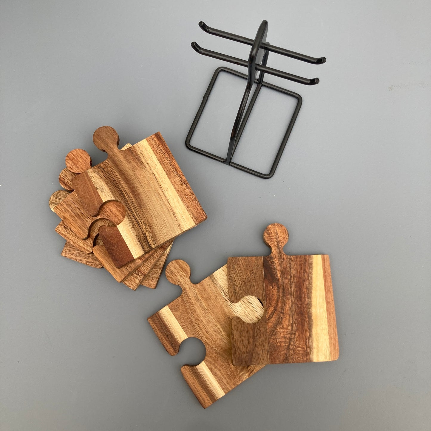 Set of 6 Acacia wood puzzle shaped coasters on a metal holder. Coasters stacked.