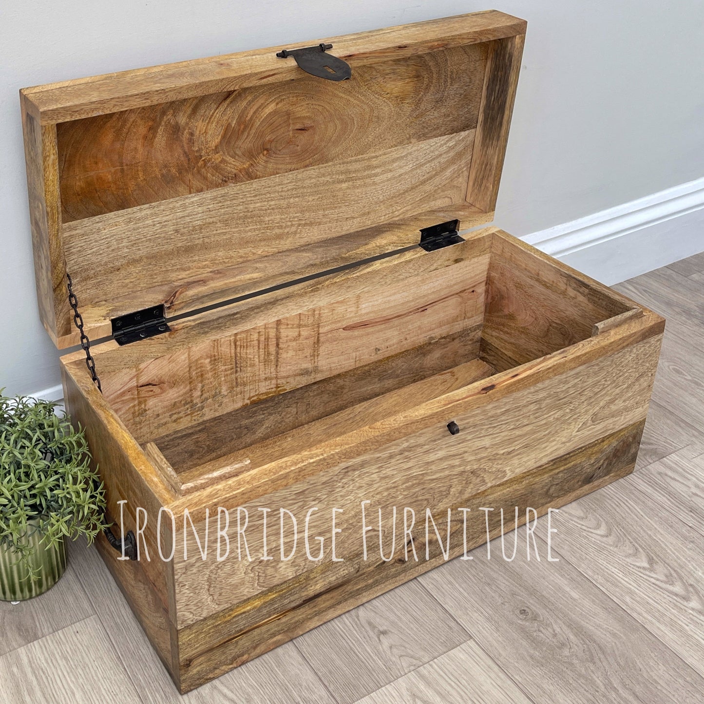 Wooden storage chest with a plant on a wooden floor, branded 'Ironbridge Furniture'.