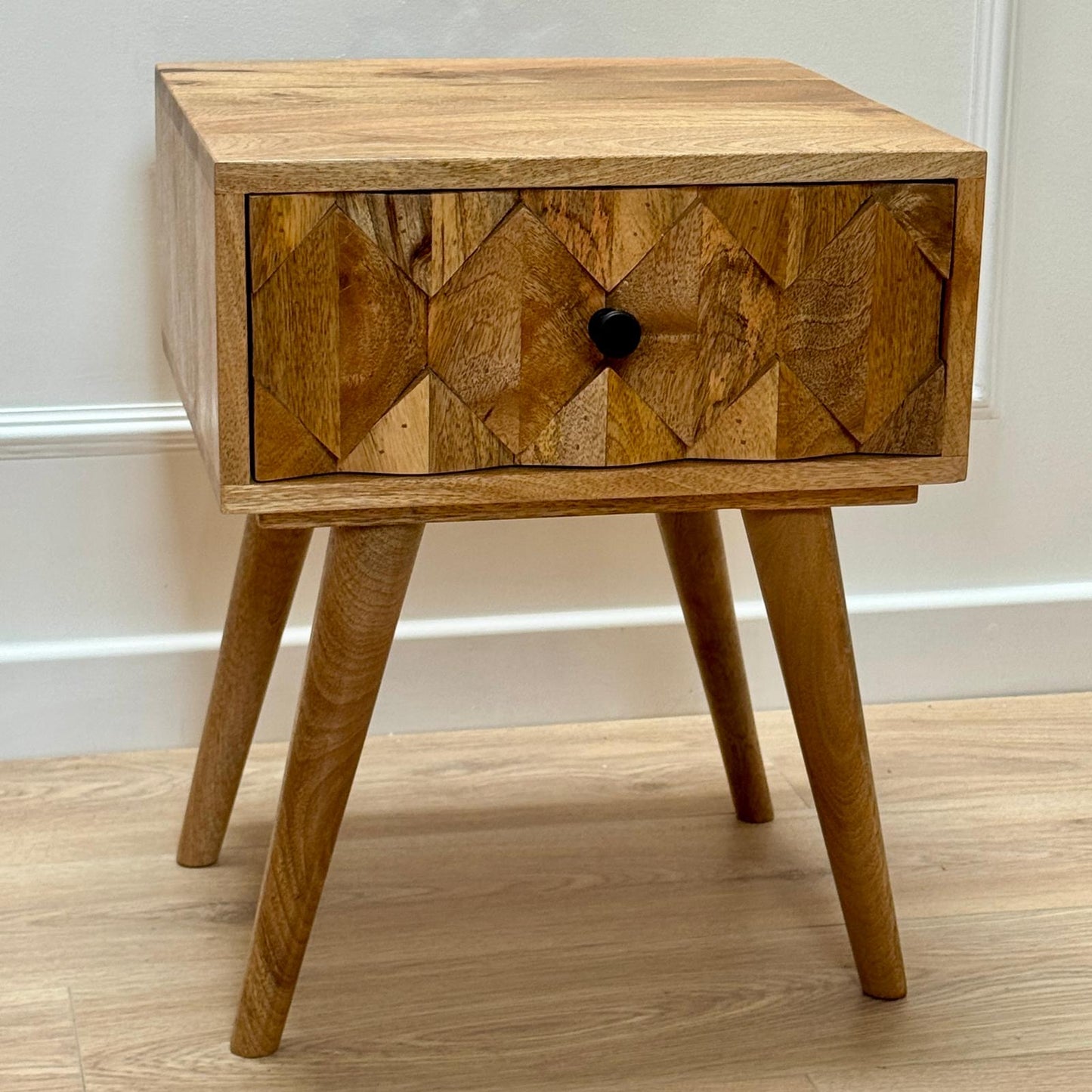 Wooden nightstand with geometric pattern on a light wooden floor.
