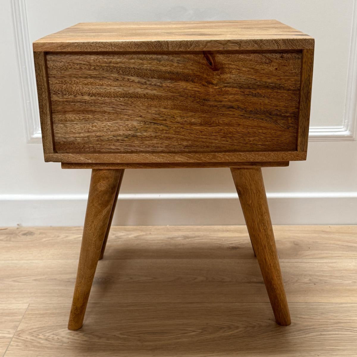 Wooden nightstand with a single drawer on a wooden floor.