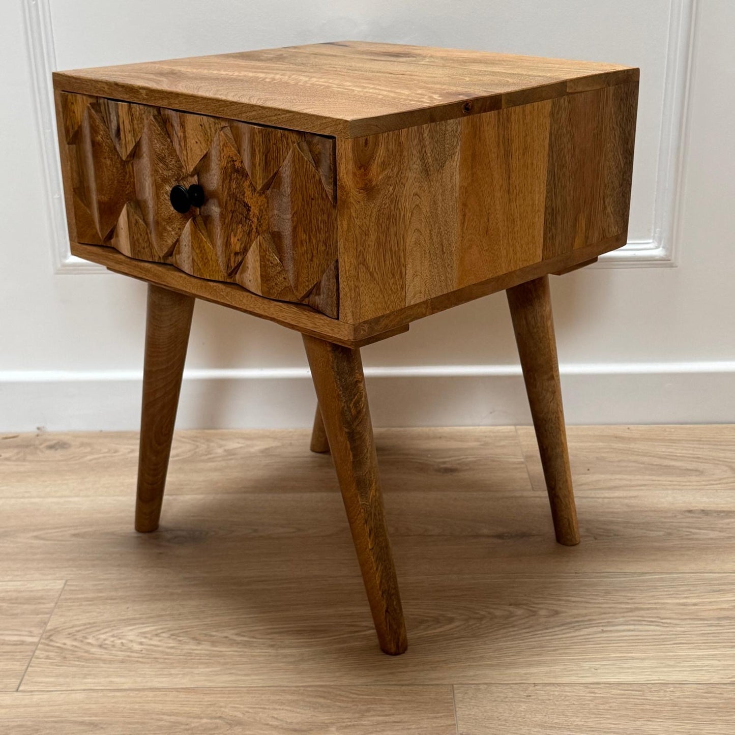 Wooden side table with a single drawer on a wooden floor.