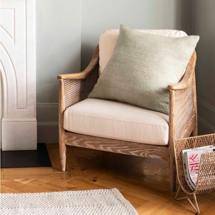 Large 60cm Herringbone wool cushion - Sage. On a chair in the corner of a room.