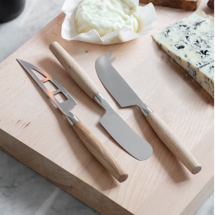 Set of cheese knives on a wooden cutting board with cheese and butter on a marble surface