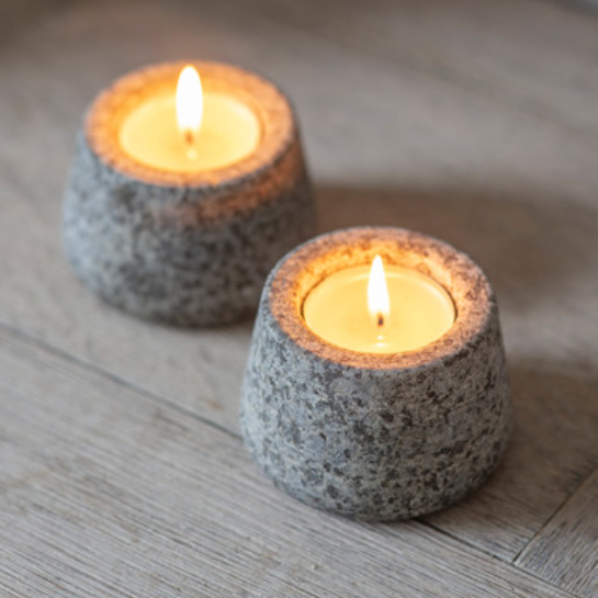 Two lit candles in textured stone holders on a wooden surface
