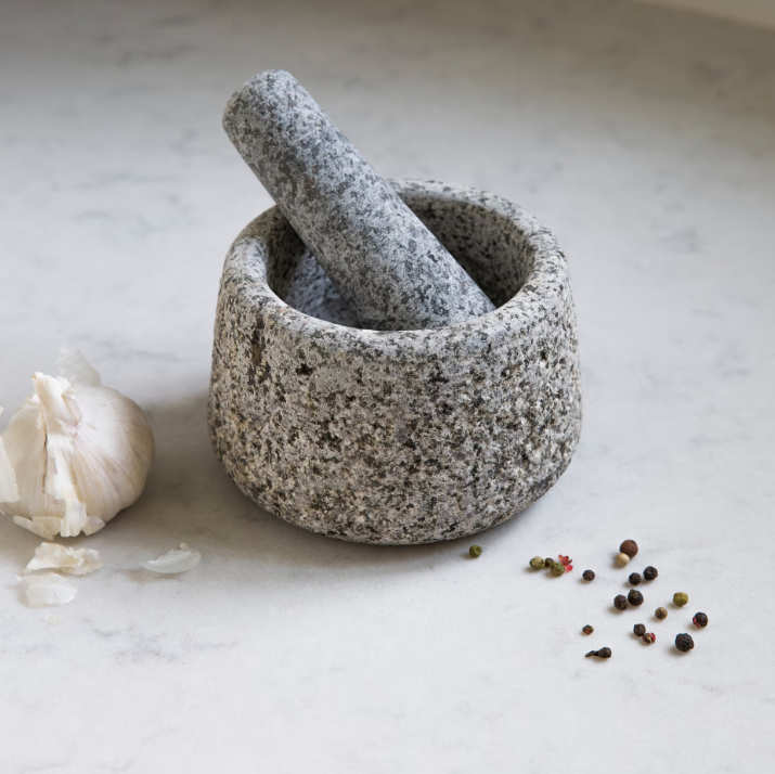 Stone mortar and pestle with garlic and peppercorns on a light surface