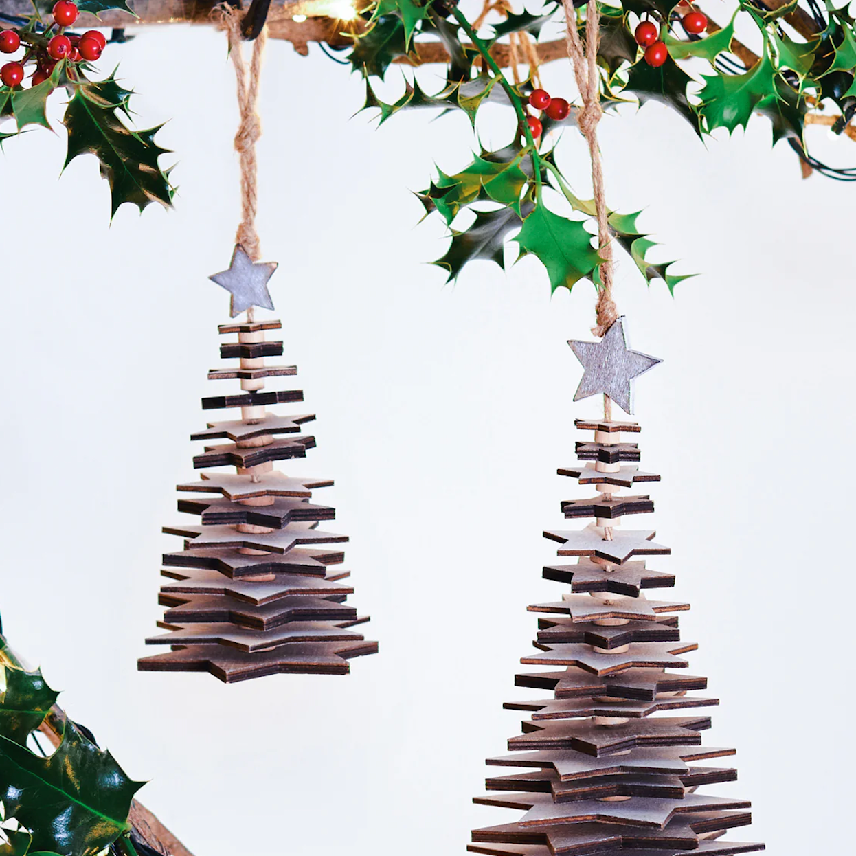 Wooden star Christmas trees - hanging from holly branch.