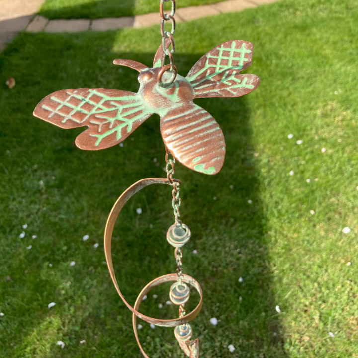 Decorative metal bee ornament on a chain against a grassy background
