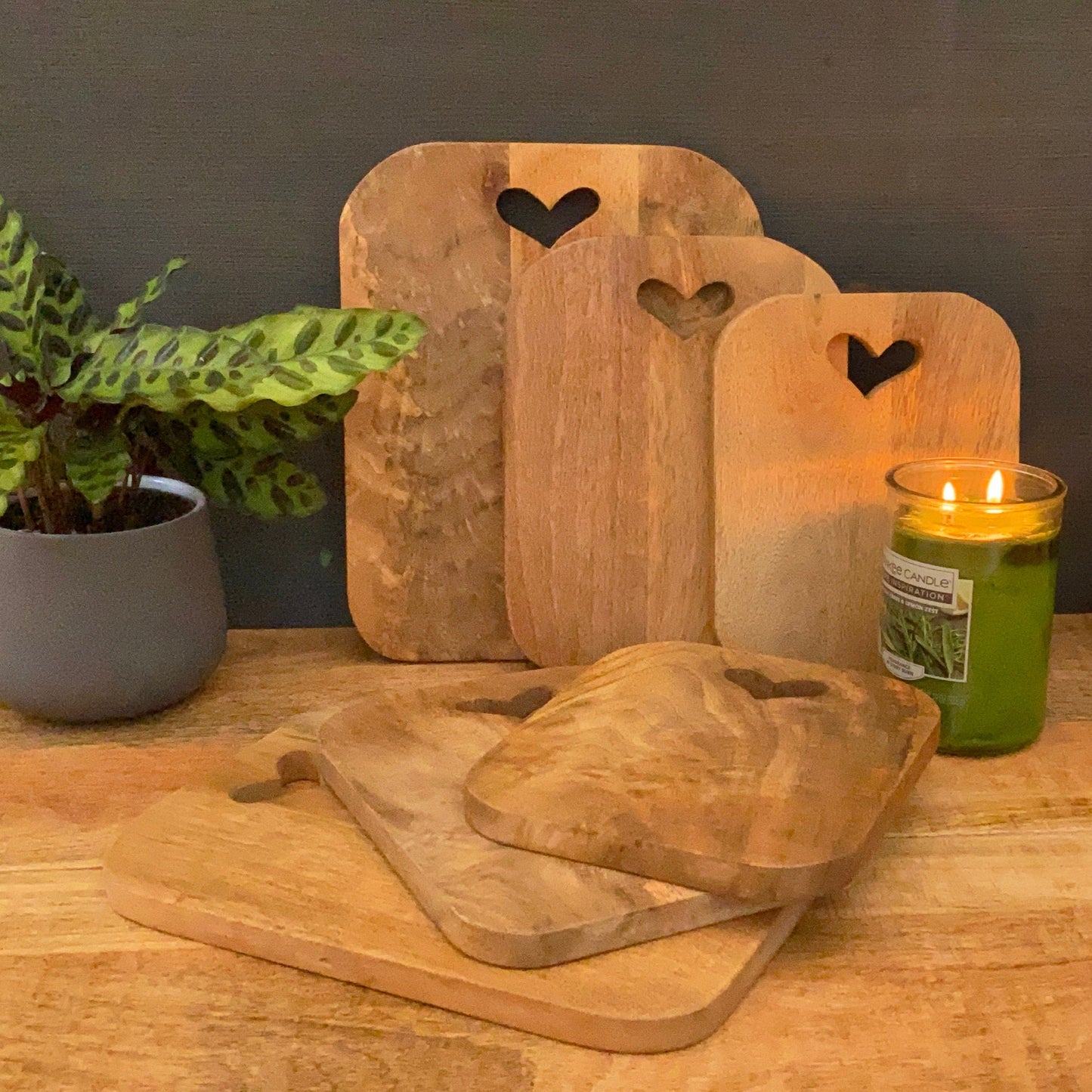 Mango wood chopping boards with cut out hearts. Shown with plant and candle.