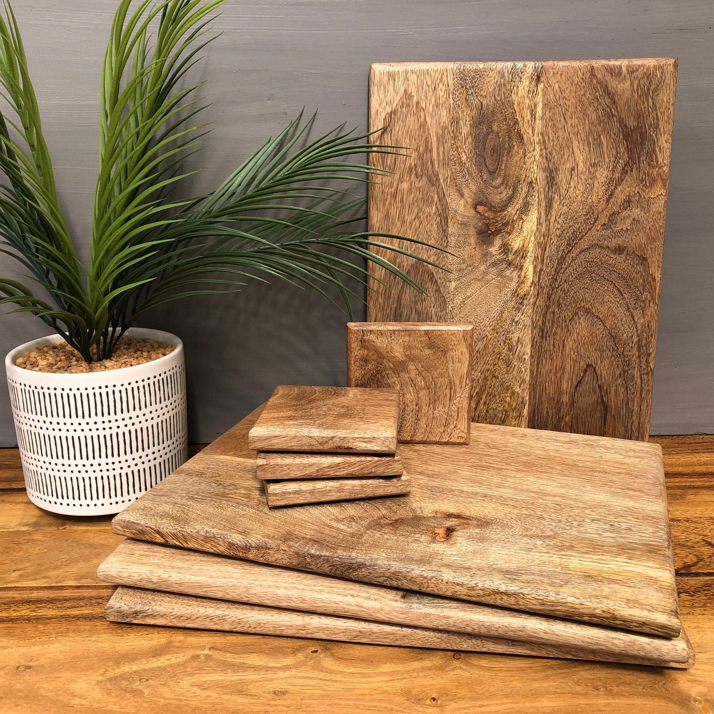 Set of Solid Mango Wood Board Placemats and Coasters. Placemats and coasters stacked with one placemat stood in the background.