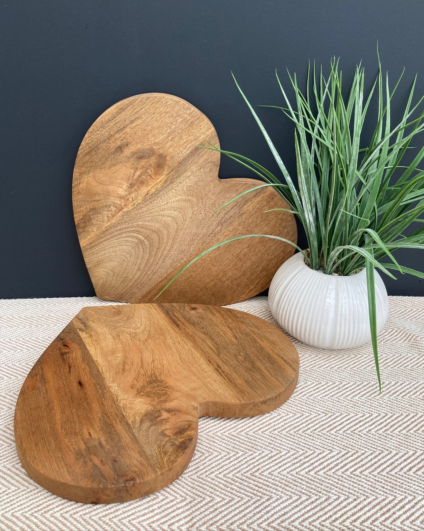 Large heart shaped Mango wood chopping board. No handle, one board on table and one board resting against wall.