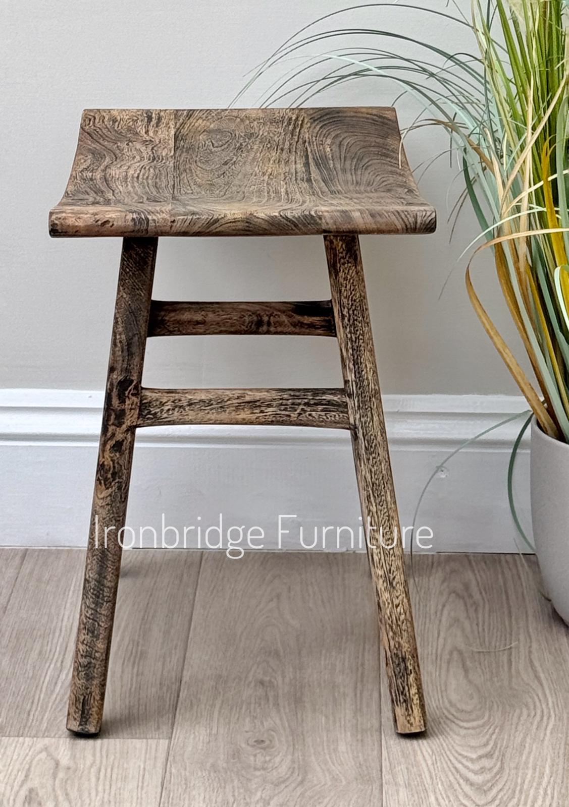 Curved rustic Mango wood stool single (dark). Side on.
