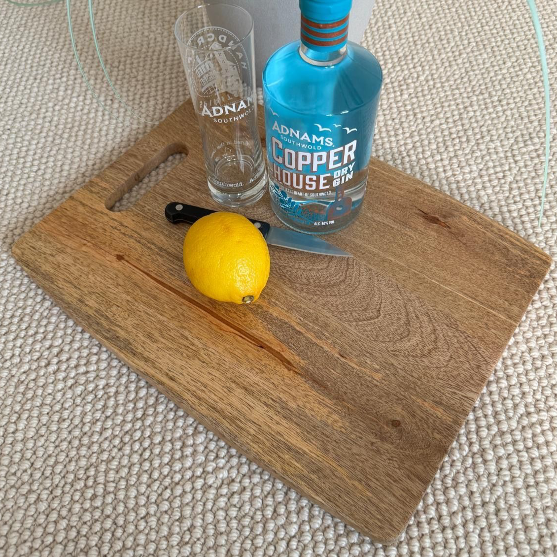 Bottle of Adnams Copper House gin with a glass and lemon on a wooden board.
