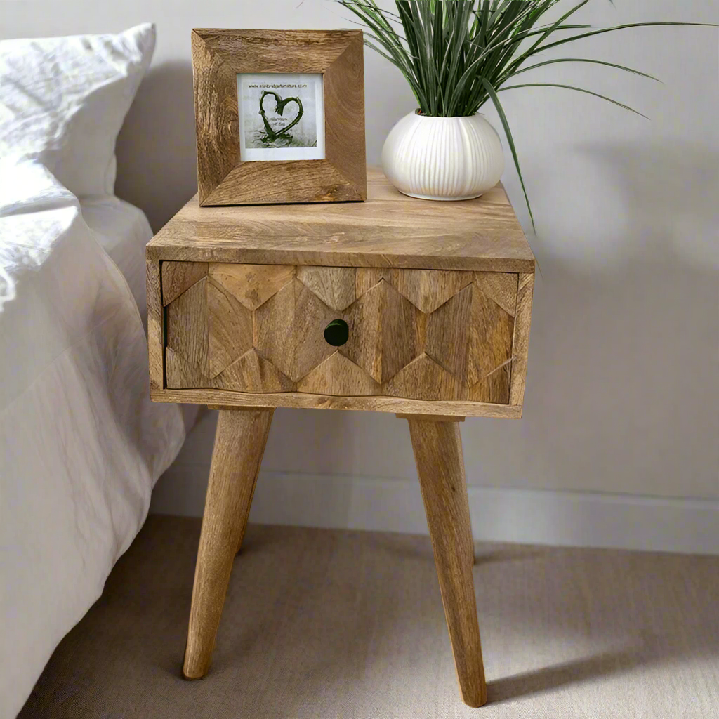 Wooden side table with geometric pattern, framed picture, and plant on a wooden floor.