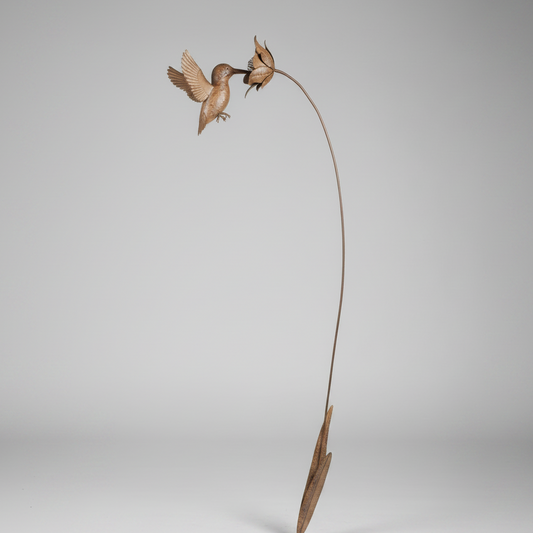 Decorative bird sculpture on a branch against a green leafy background