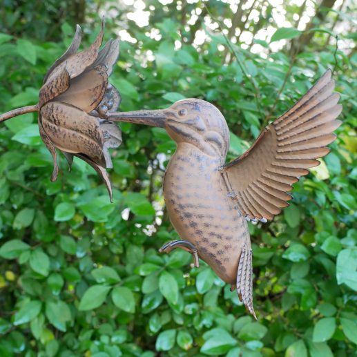 Decorative metal sculpture of a bird and a flower against a green leafy background