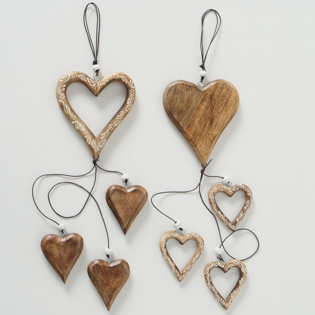 Two heart-shaped wooden wall hanging ornaments displayed against a light gray background. Each ornament features a larger central heart and smaller dangling hearts, crafted from natural wood with some pieces showing carved floral patterns.