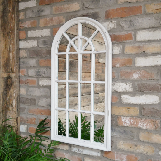 White arched window-style mirror on a brick wall with plants below