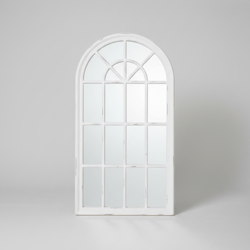 Decorative white window-shaped mirror on a brick wall with plants below.