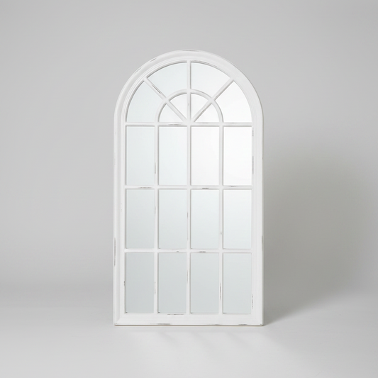 Decorative white window-shaped mirror on a brick wall with plants below.