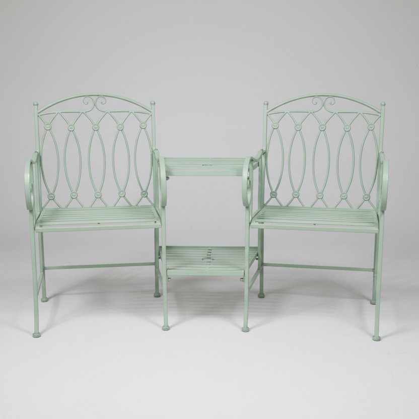 Two white metal garden chairs and a table set against a stone wall.