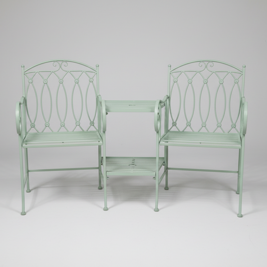 Two white metal garden chairs and a table set against a stone wall.